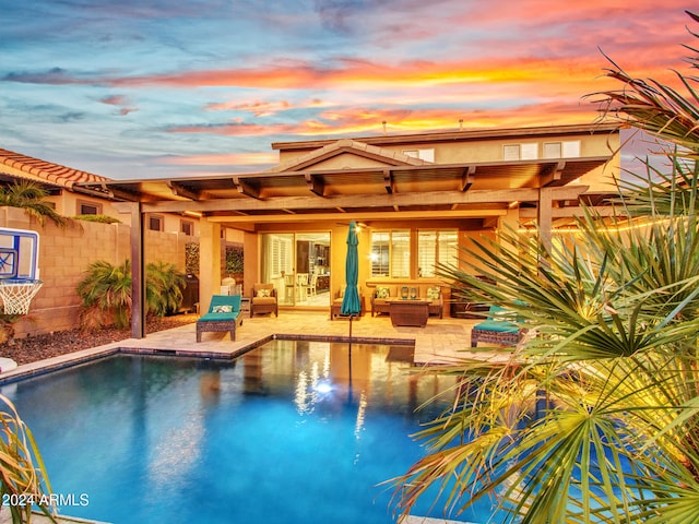 pool at dusk with outdoor lounge area and a patio