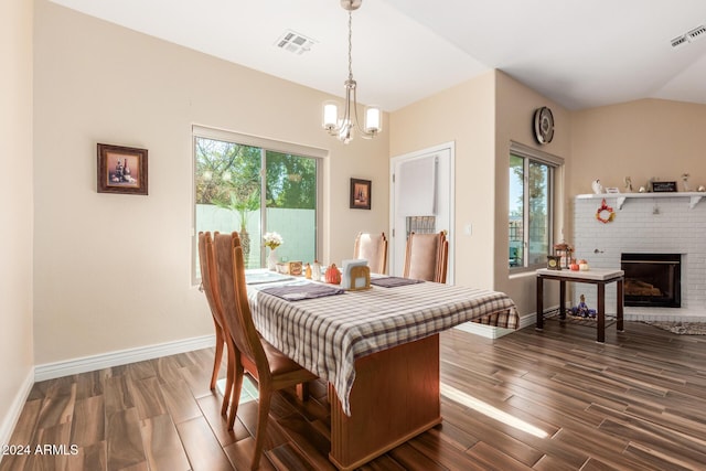 dining space featuring an inviting chandelier, dark wood-type flooring, lofted ceiling, and a brick fireplace