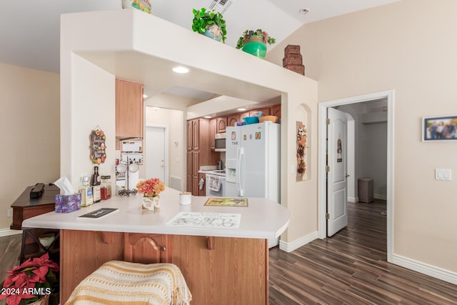 kitchen featuring white appliances, a kitchen breakfast bar, vaulted ceiling, dark hardwood / wood-style flooring, and kitchen peninsula