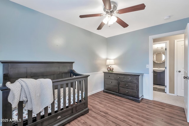 bedroom with light wood-type flooring, ensuite bathroom, ceiling fan, sink, and a crib