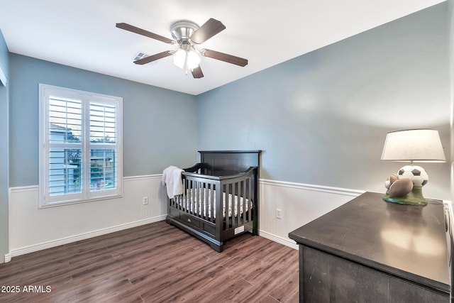 bedroom with ceiling fan, dark hardwood / wood-style flooring, and a nursery area