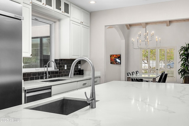 kitchen with decorative backsplash, dishwashing machine, glass insert cabinets, light stone countertops, and white cabinetry