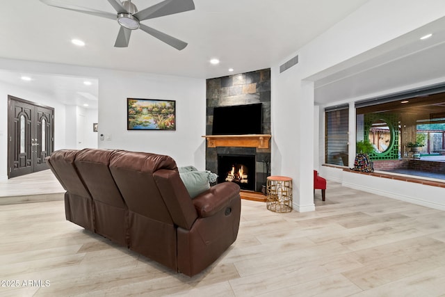 living room with a tile fireplace, light hardwood / wood-style floors, and ceiling fan