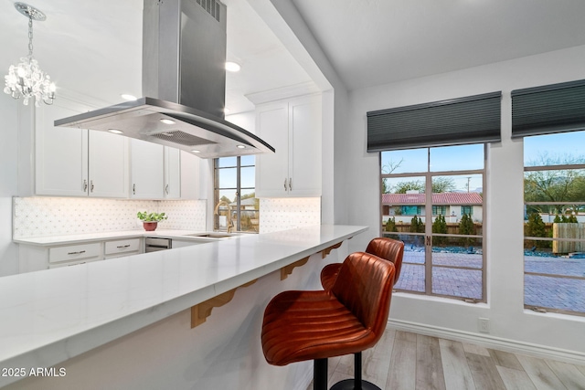 kitchen with white cabinetry, island exhaust hood, a breakfast bar, and backsplash