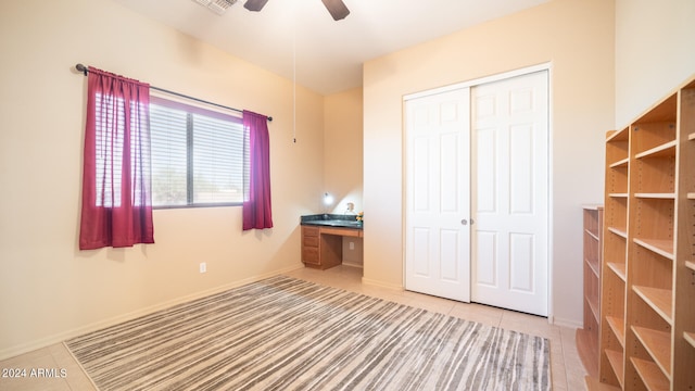 unfurnished bedroom with a closet, built in desk, tile patterned floors, and ceiling fan