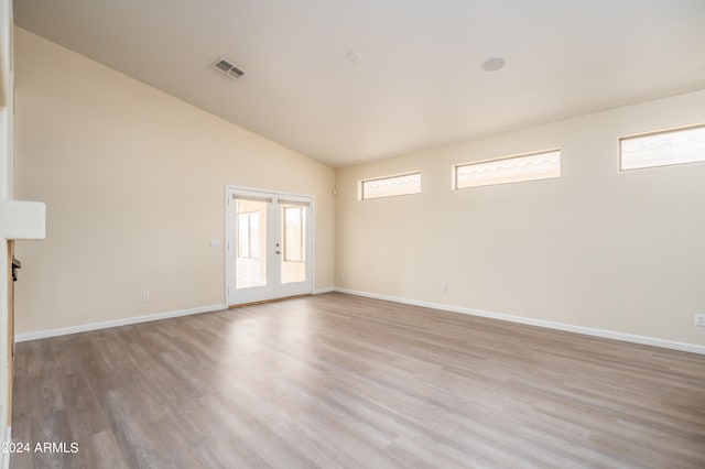 empty room featuring light hardwood / wood-style floors, high vaulted ceiling, and french doors