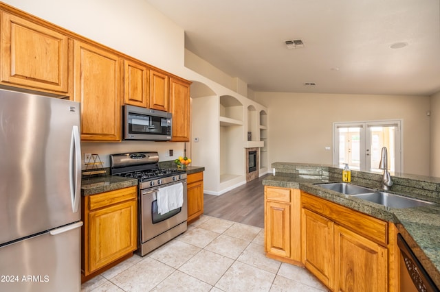 kitchen with appliances with stainless steel finishes, light hardwood / wood-style floors, french doors, sink, and vaulted ceiling