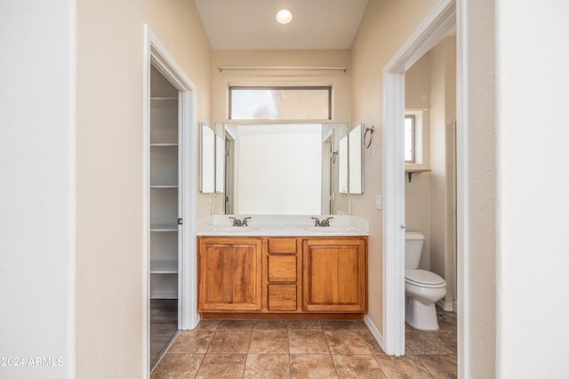 bathroom with a healthy amount of sunlight, dual sinks, tile flooring, toilet, and large vanity