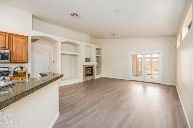 unfurnished living room featuring a tiled fireplace, lofted ceiling, built in features, french doors, and hardwood / wood-style flooring