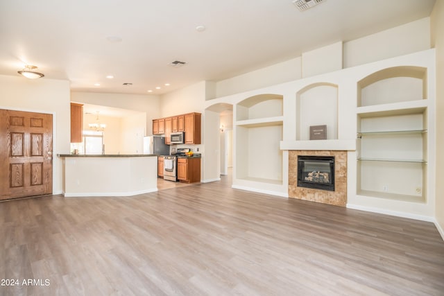 unfurnished living room with built in features, a chandelier, light hardwood / wood-style floors, and a fireplace