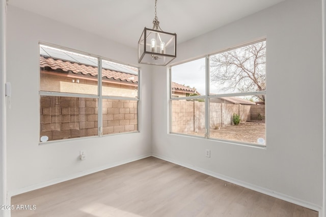 unfurnished dining area with a chandelier, a healthy amount of sunlight, baseboards, and wood finished floors