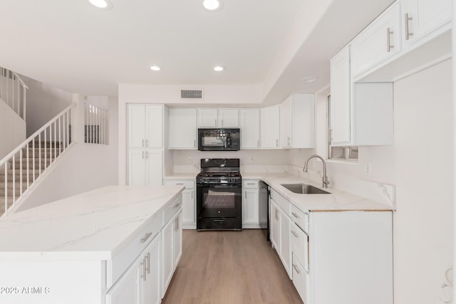 kitchen with light stone counters, visible vents, a sink, black appliances, and light wood-style floors