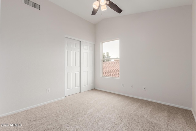 unfurnished bedroom with baseboards, visible vents, vaulted ceiling, a closet, and light carpet