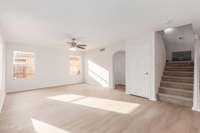 unfurnished room with light wood finished floors, visible vents, ceiling fan, stairway, and arched walkways