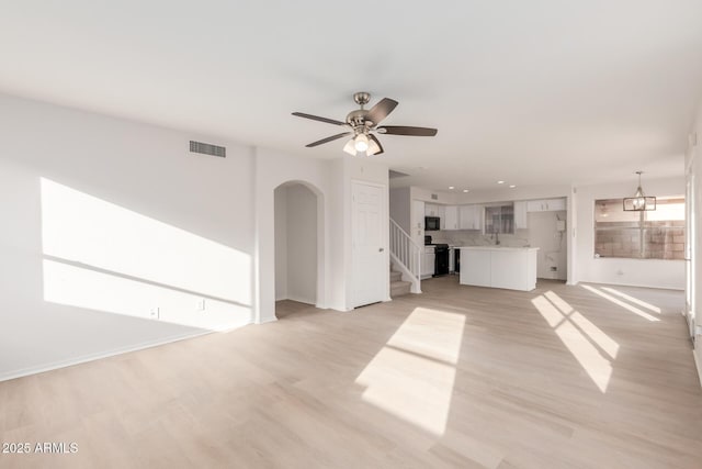 unfurnished living room with stairs, light wood-type flooring, arched walkways, and ceiling fan