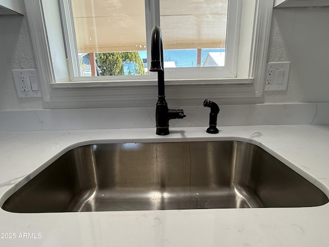 interior details featuring a sink, light stone counters, and a textured wall