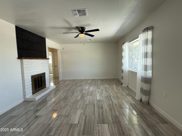 unfurnished living room featuring wood finished floors, a ceiling fan, visible vents, baseboards, and a brick fireplace