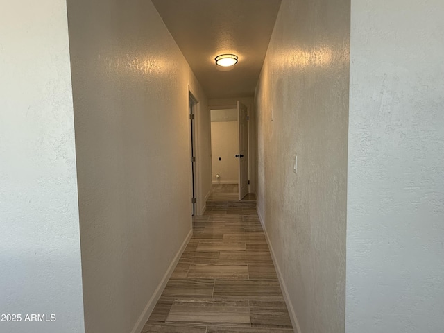 corridor with wood finish floors, baseboards, and a textured wall