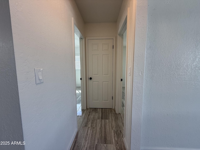 hallway featuring baseboards, wood finished floors, and a textured wall