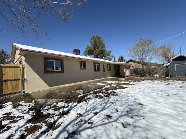 snow covered property with fence, central AC, stucco siding, an outbuilding, and a storage unit