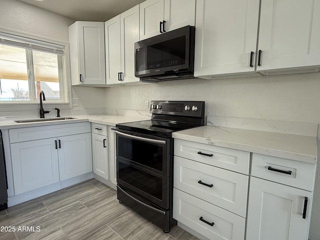 kitchen with range with two ovens, light stone counters, a textured wall, white cabinets, and a sink