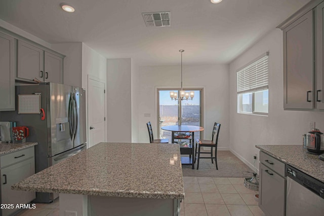 kitchen featuring appliances with stainless steel finishes, a kitchen island, a notable chandelier, pendant lighting, and light stone countertops