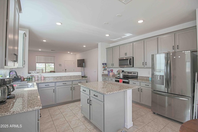 kitchen with stainless steel appliances, a center island, sink, and light stone countertops