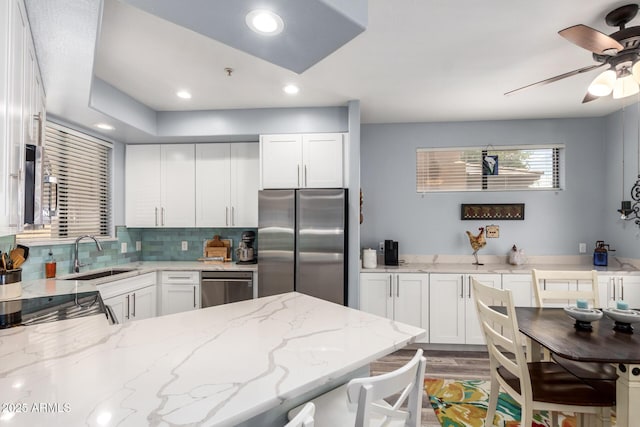 kitchen featuring stainless steel appliances, a sink, white cabinets, backsplash, and light stone countertops