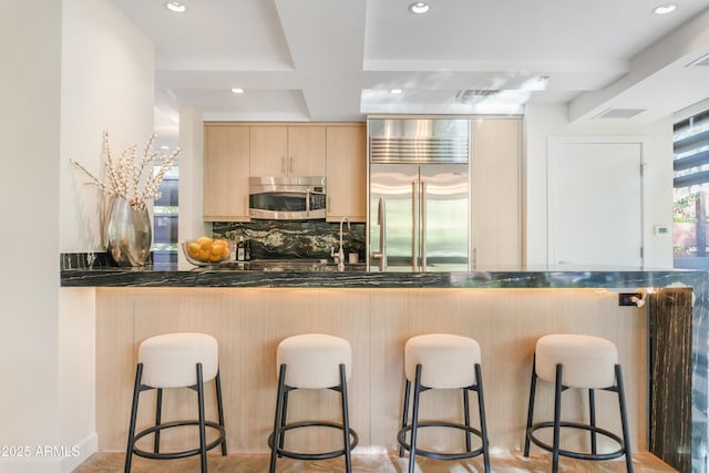 7117 E Rancho Vista Dr Unit 1012, Scottsdale, AZ 85251 - kitchen featuring appliances with stainless steel finishes, light brown cabinets, dark countertops, decorative backsplash, and a kitchen bar
