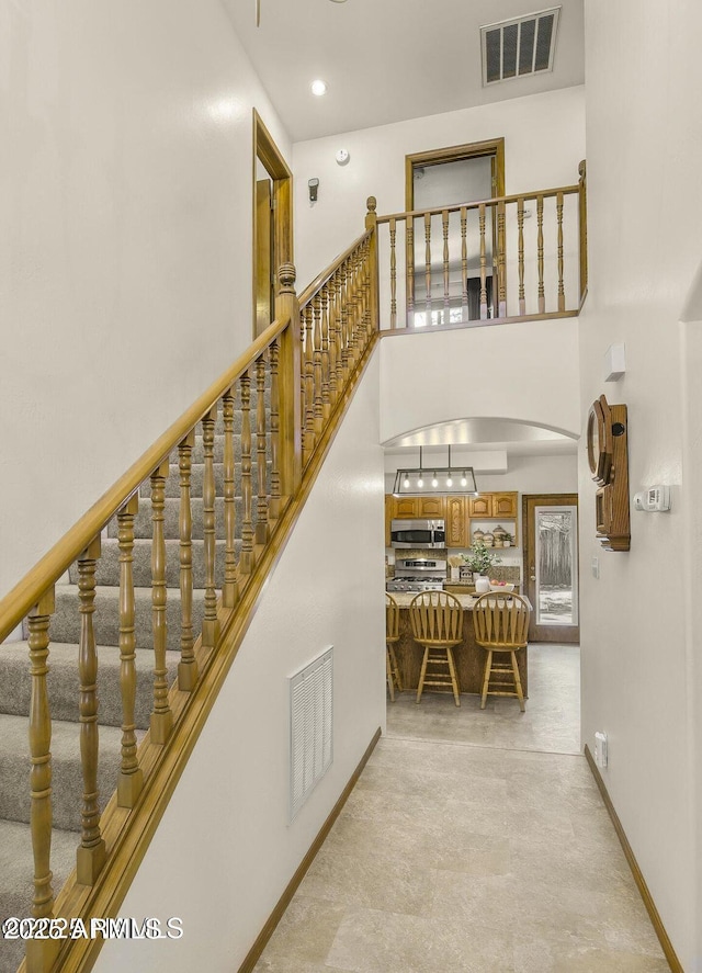 stairs with a high ceiling, arched walkways, baseboards, and visible vents