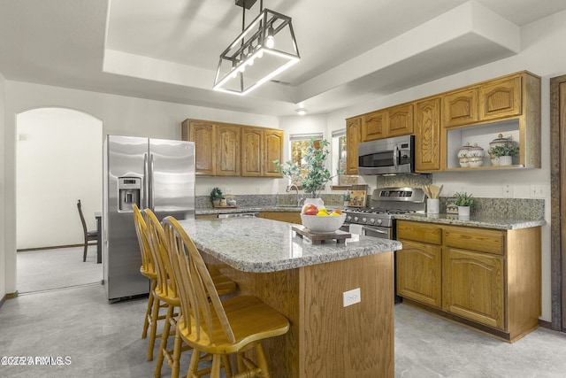 kitchen with a center island, a raised ceiling, a sink, arched walkways, and appliances with stainless steel finishes