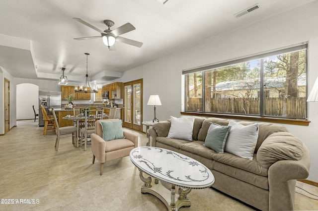 living area featuring arched walkways, ceiling fan, and visible vents