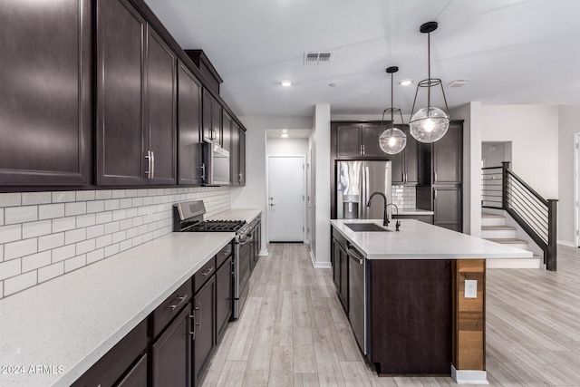 kitchen featuring dark brown cabinetry, sink, hanging light fixtures, stainless steel appliances, and a kitchen island with sink