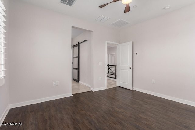 empty room with ceiling fan, a barn door, and dark hardwood / wood-style flooring