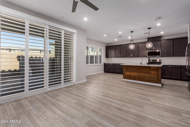 kitchen featuring appliances with stainless steel finishes, an island with sink, backsplash, hanging light fixtures, and dark brown cabinets