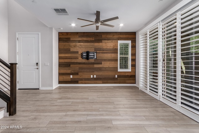 interior space featuring light hardwood / wood-style floors, ceiling fan, and wood walls