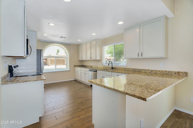 kitchen featuring stainless steel appliances, a sink, a peninsula, baseboards, and light stone counters