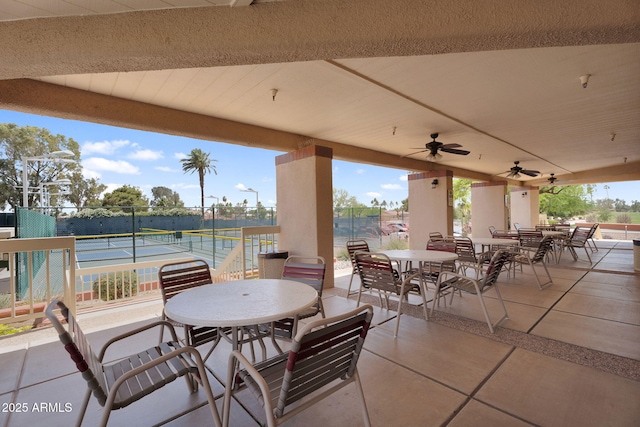 view of patio featuring outdoor dining area, fence, a ceiling fan, and a tennis court