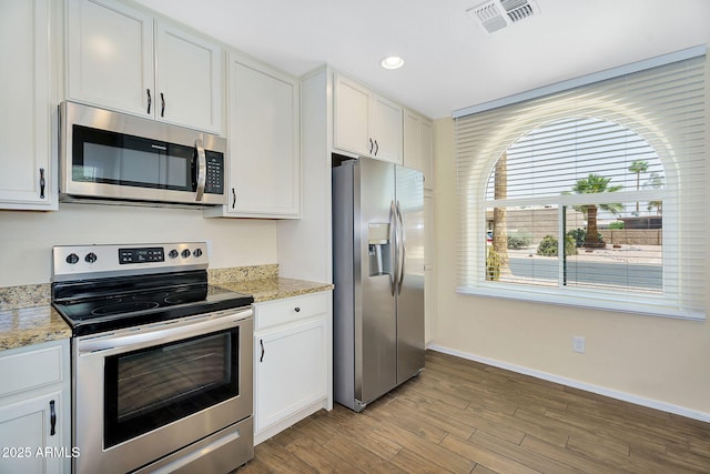 kitchen with appliances with stainless steel finishes, baseboards, white cabinets, wood finished floors, and light stone countertops