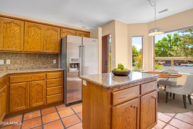 kitchen with a center island, decorative light fixtures, light stone counters, decorative backsplash, and stainless steel fridge with ice dispenser