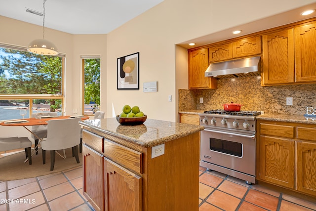 kitchen with pendant lighting, backsplash, light stone counters, a kitchen island, and premium stove