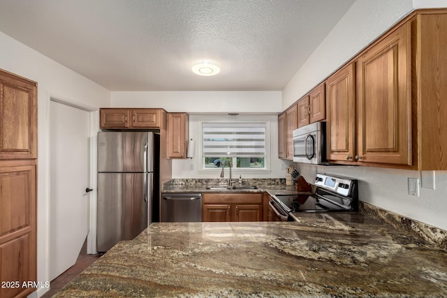 kitchen with dark stone counters, stainless steel appliances, a sink, and brown cabinets