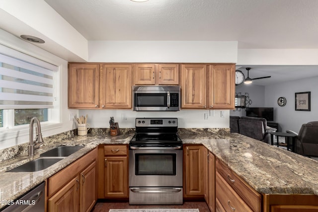 kitchen featuring dark stone counters, appliances with stainless steel finishes, brown cabinetry, and a sink