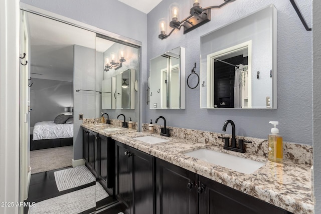 ensuite bathroom with a textured wall, connected bathroom, a sink, and double vanity