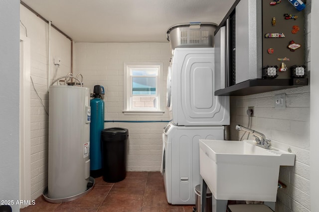 laundry room with laundry area, dark tile patterned floors, a sink, and stacked washer / drying machine