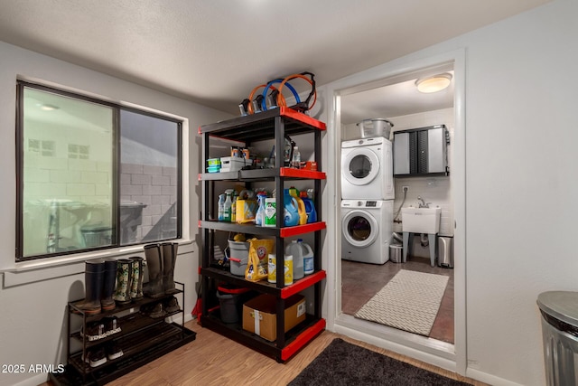 laundry area with a sink, laundry area, stacked washer / dryer, and wood finished floors