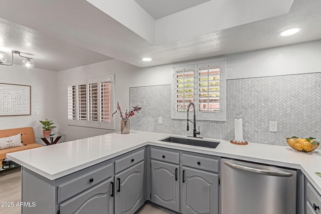 kitchen featuring a peninsula, light countertops, a sink, dishwasher, and gray cabinetry