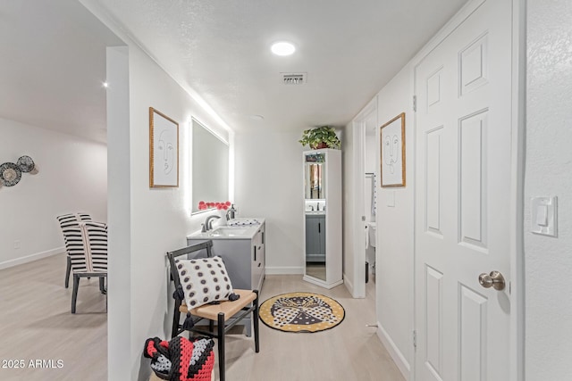 hall with visible vents, a sink, baseboards, and light wood-type flooring