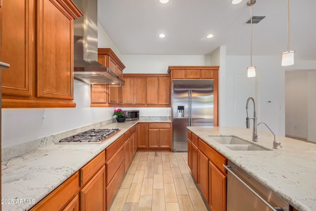 kitchen with sink, wall chimney exhaust hood, appliances with stainless steel finishes, decorative light fixtures, and light stone counters