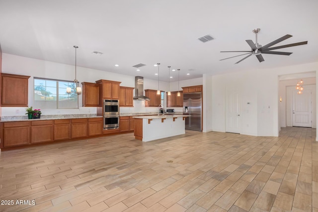 kitchen with a kitchen bar, stainless steel appliances, wall chimney range hood, a center island, and hanging light fixtures